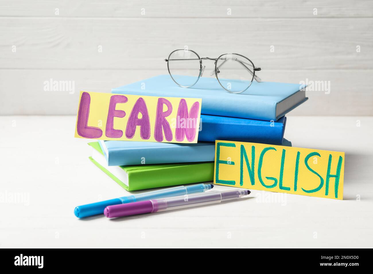 Phrase LEARN ENGLISH, books, glasses and felt tip pens on white wooden table Stock Photo