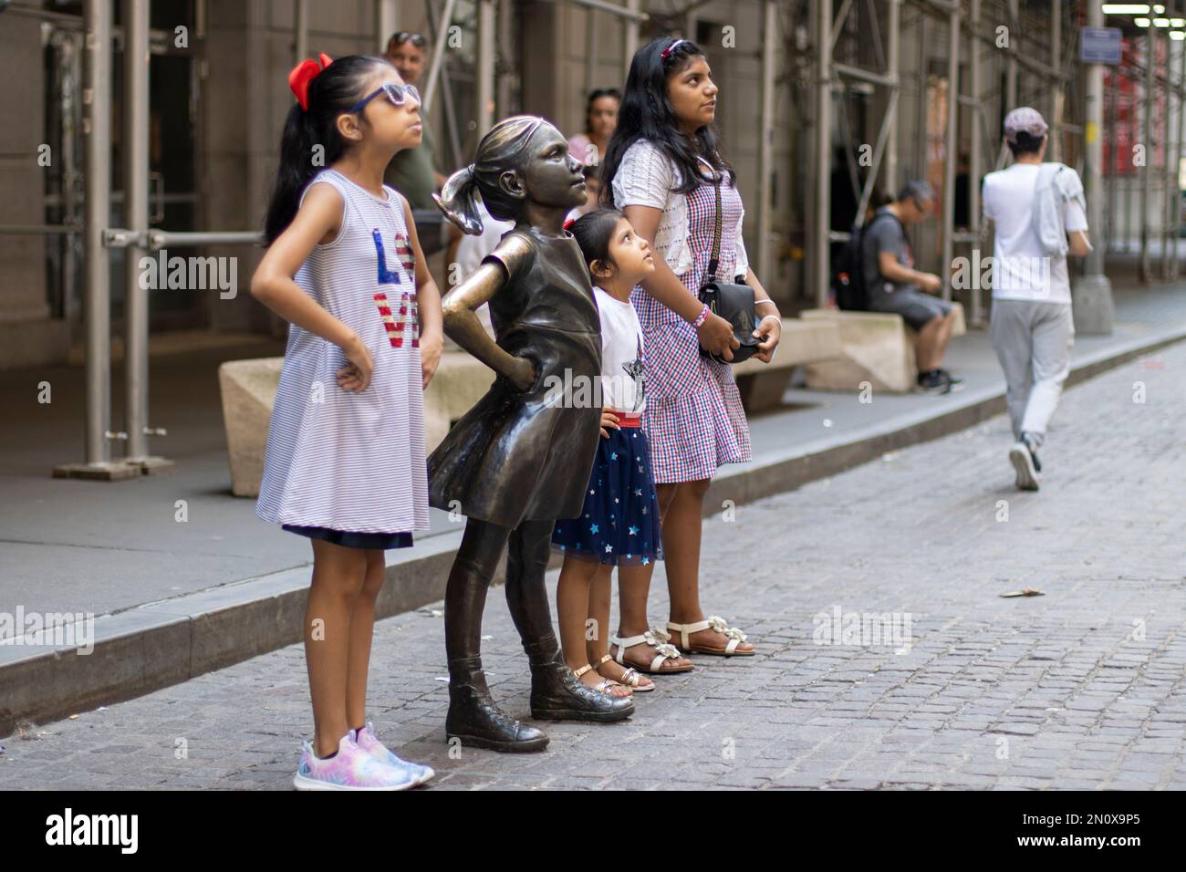 Young visitors to the Financial District of Manhattan, New York City, pose with the Fearless Girl statue facing the New York Stock Exchange Building ... Stock Photo