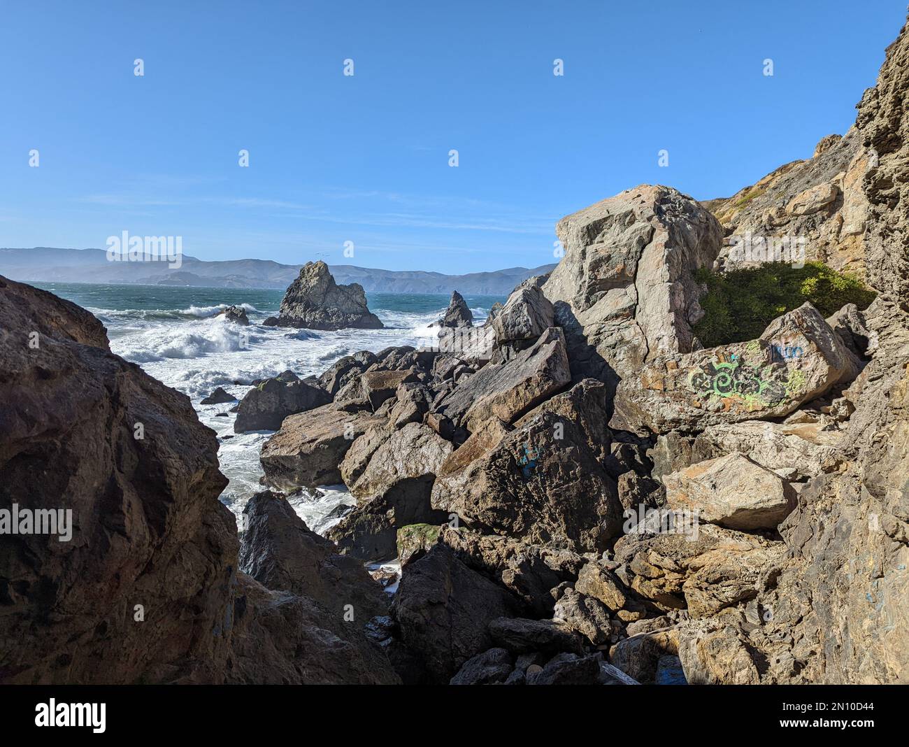 The foamy waves of an ocean hitting the rocks on the shore with the ...