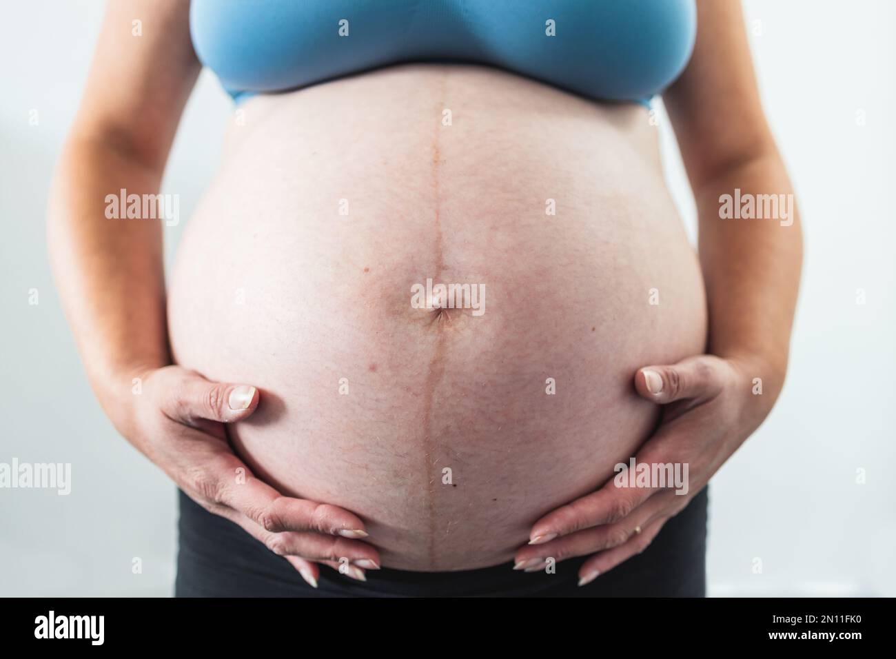 pregnant woman touching her bump in the latest stage of pregnancy, mid-section showing the belly and body shape with no face in the frame Stock Photo