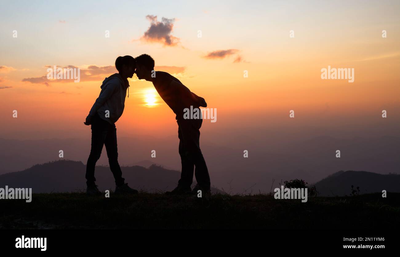 Silhouette of a couple on the mountain, A young romantic couple enjoy a beautiful view of the sun setting over the mountains, love, Valentine's Day. Stock Photo
