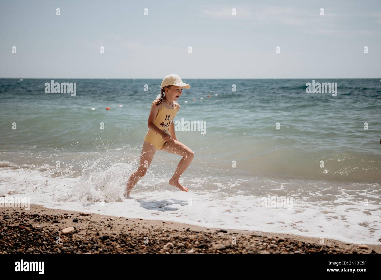 Cute little girl running along the seashore against a clear blue sea
