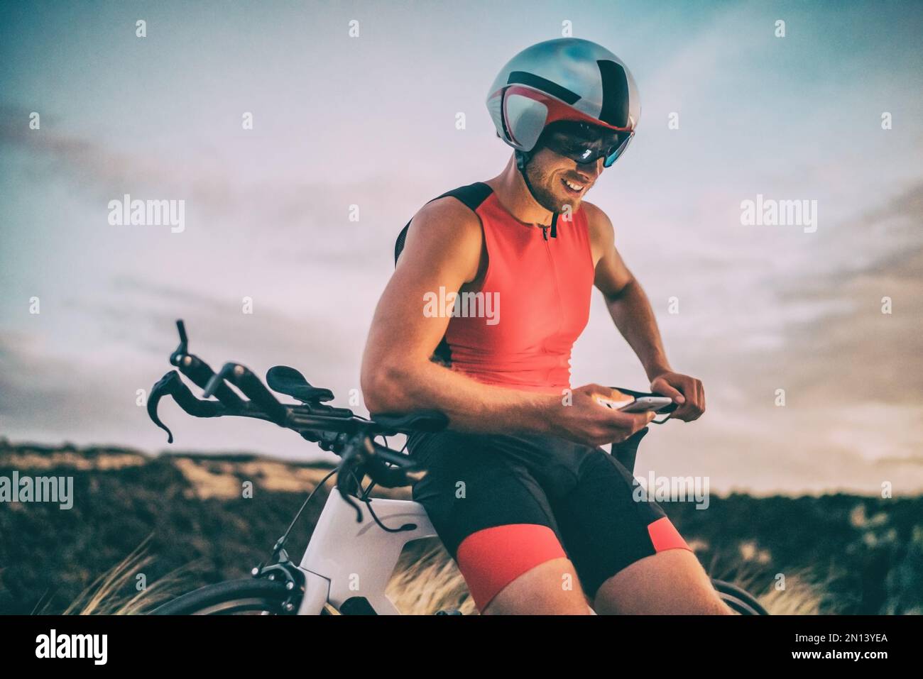 Triathlon cyclist athlete man using health monitor sports app on mobile  phone after bike training. Triathlete at dusk wearing tri suit and helmet  on Stock Photo - Alamy