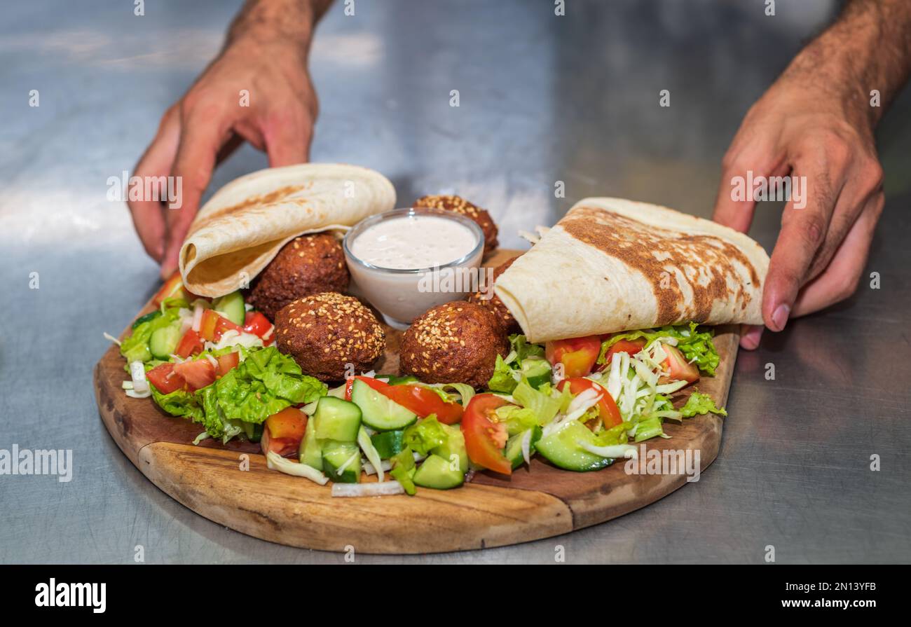 Presenting the middle eastern Lebanese dish Falafel on a wooden plate. tortilla, vegetable salad, and tahini sauce. Stock Photo