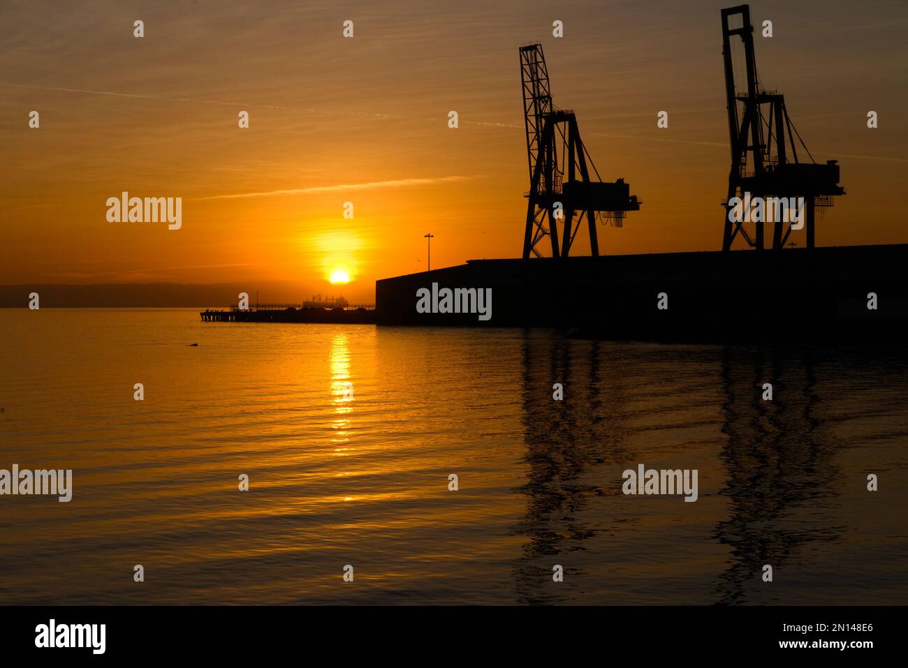 Two container cranes on waterfront of San Francisco Bay with reflection in water Stock Photo