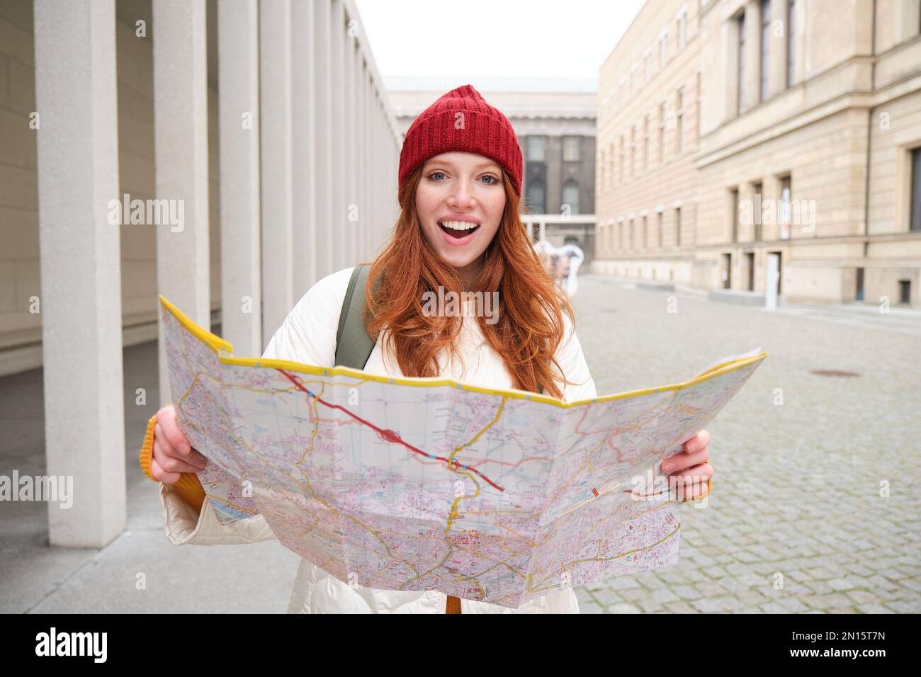 Beautiful redhead woman, tourist with city map, explores sightseeing historical landmark, walking around old town, smiling happily. Stock Photo