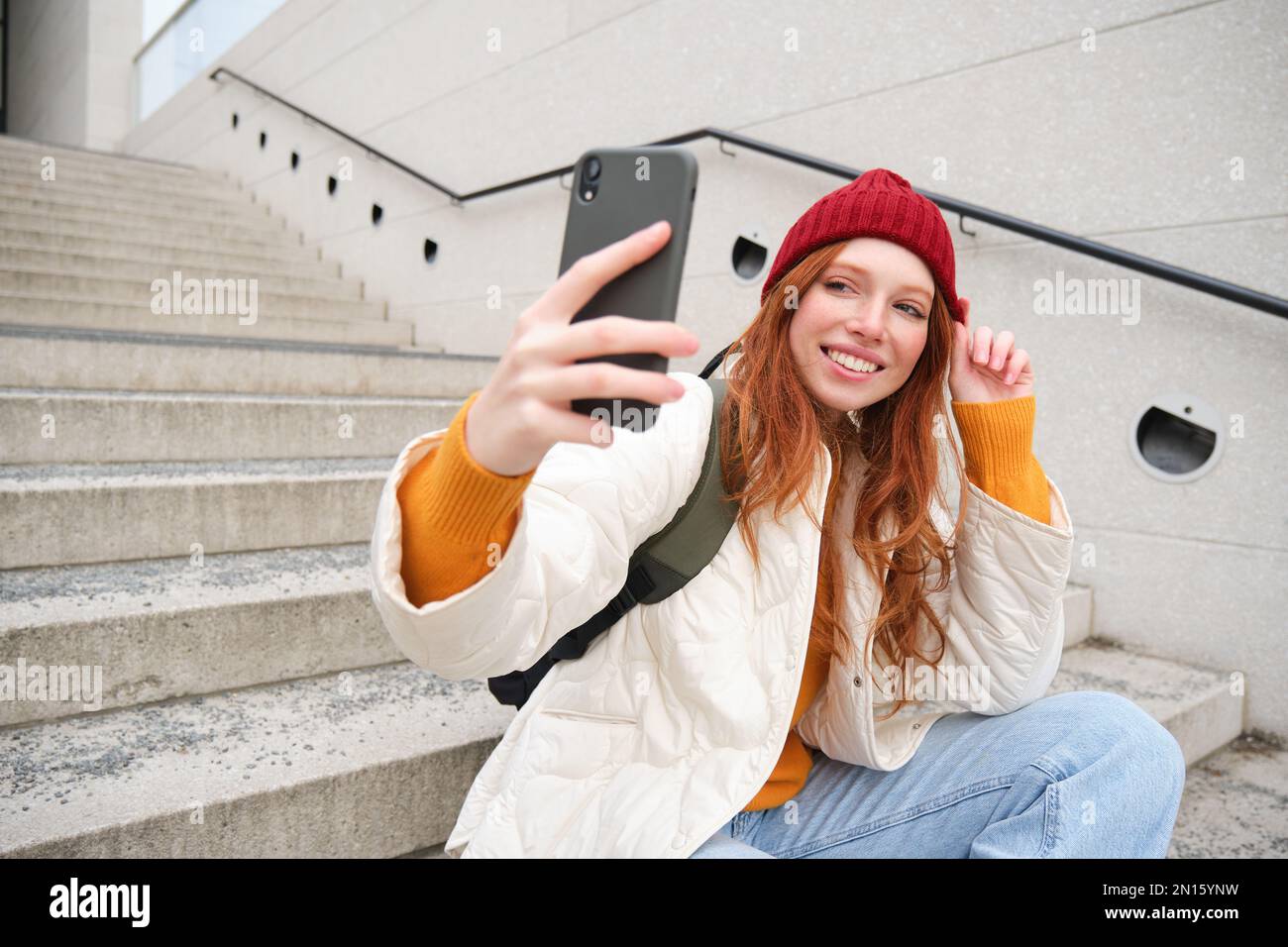 Urban girl takes selfie on street stairs, uses smartphone app to take photo of herself, poses for social media application. Stock Photo