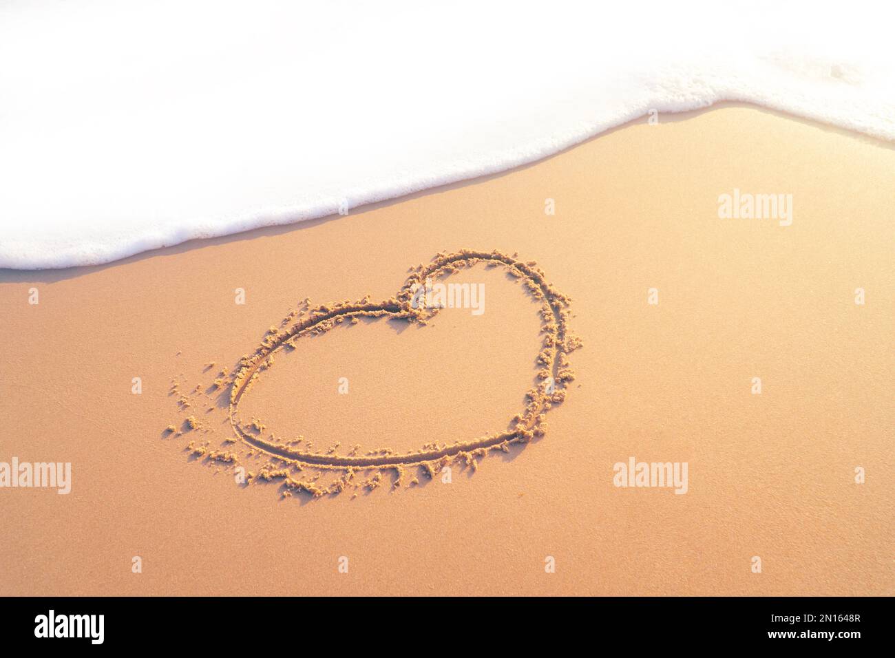 Draw a heart shape on the sandy beach by hand in the morning. to welcome Valentine's Day festival. Stock Photo