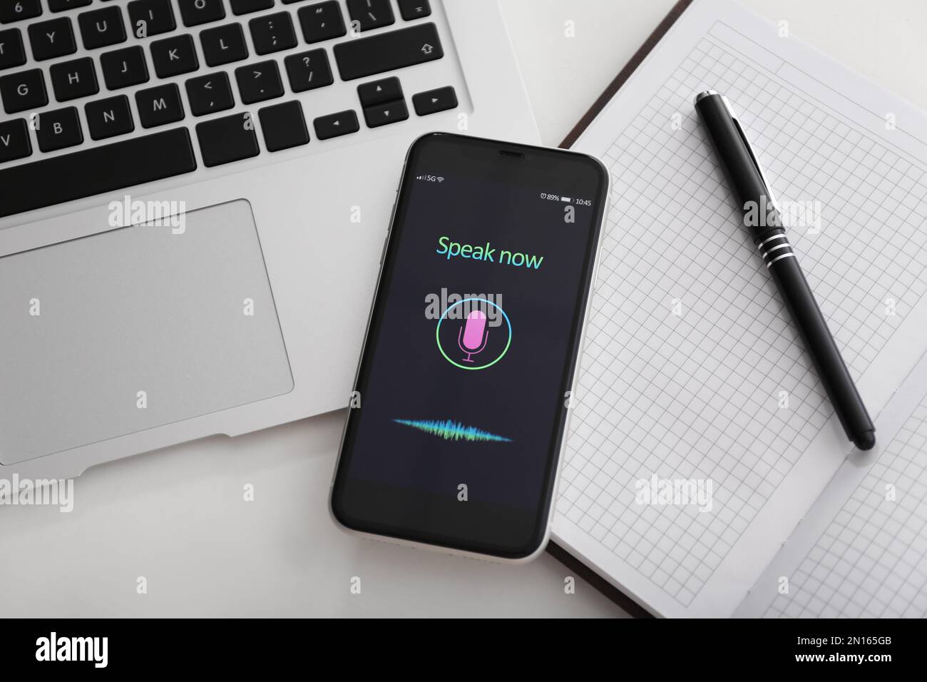 Smartphone with activated voice search app, laptop and stationery on white table, flat lay Stock Photo