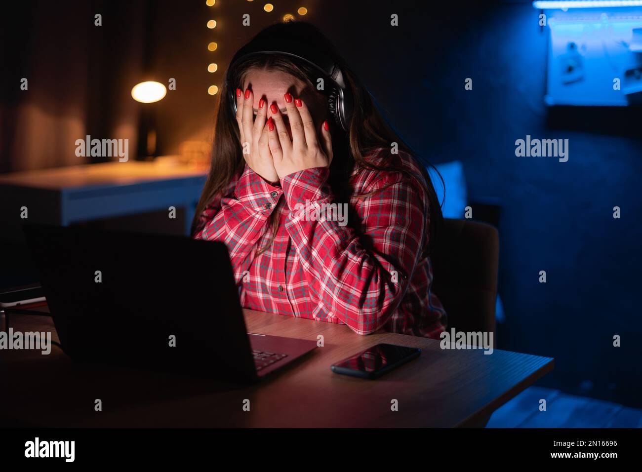 Young female watching scary movie, hiding face in fear. Horror movie at home. Online film service Stock Photo