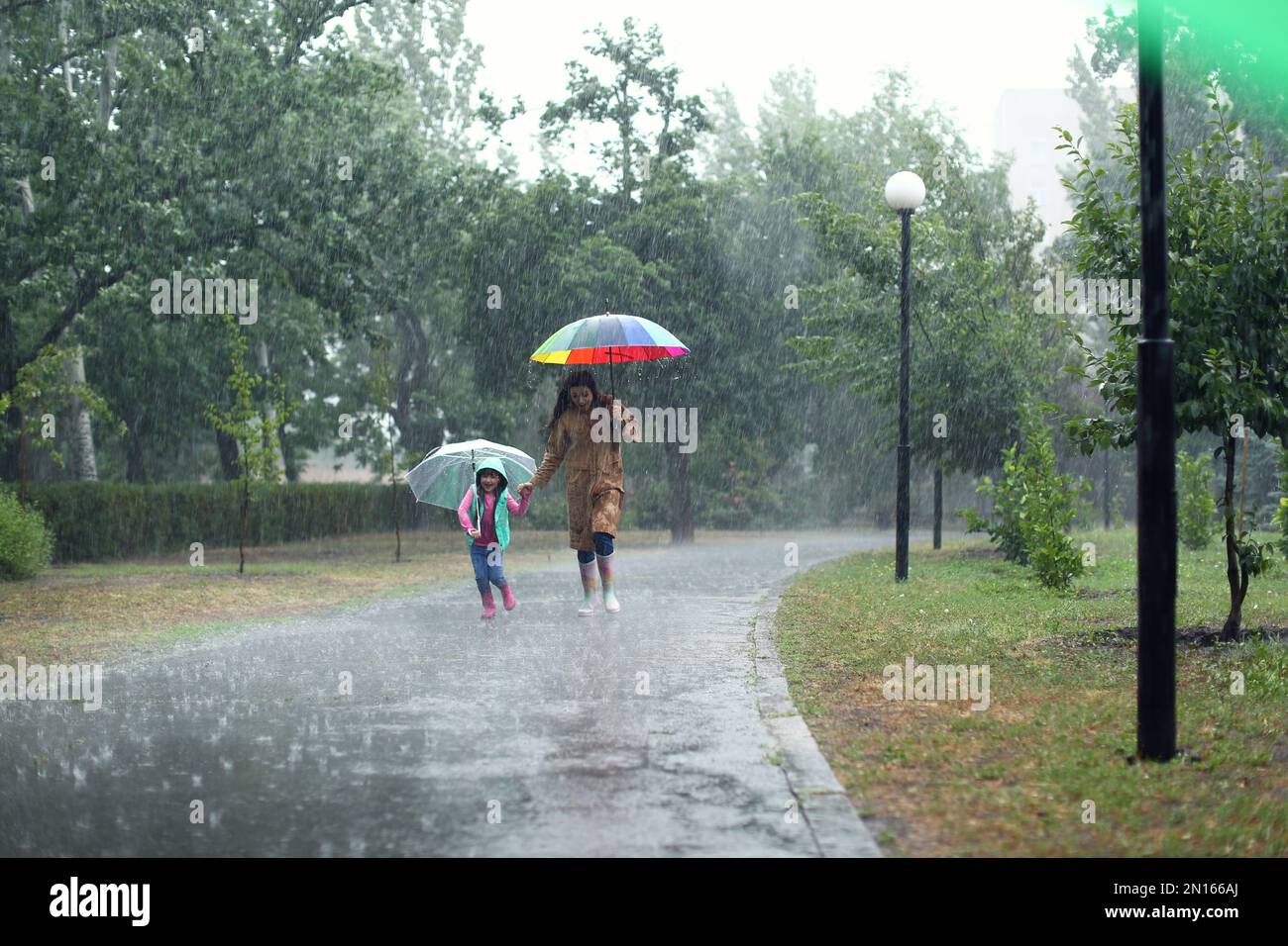 Mother and her daughter with umbrellas running outdoors on rainy day ...