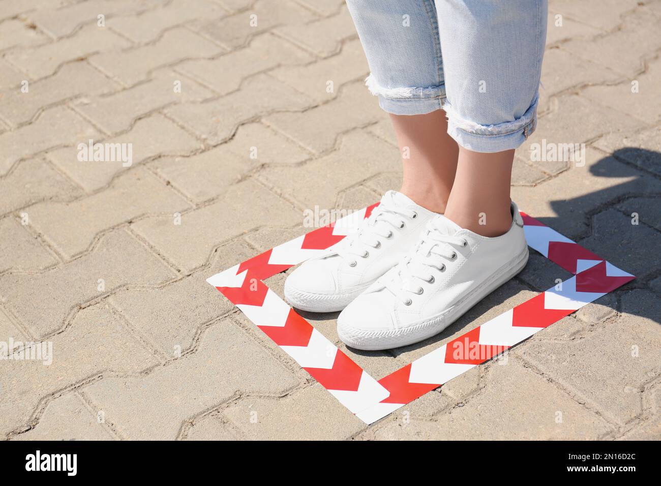 Woman standing on taped floor marking for social distance outdoors, closeup with space for text. Coronavirus pandemic Stock Photo