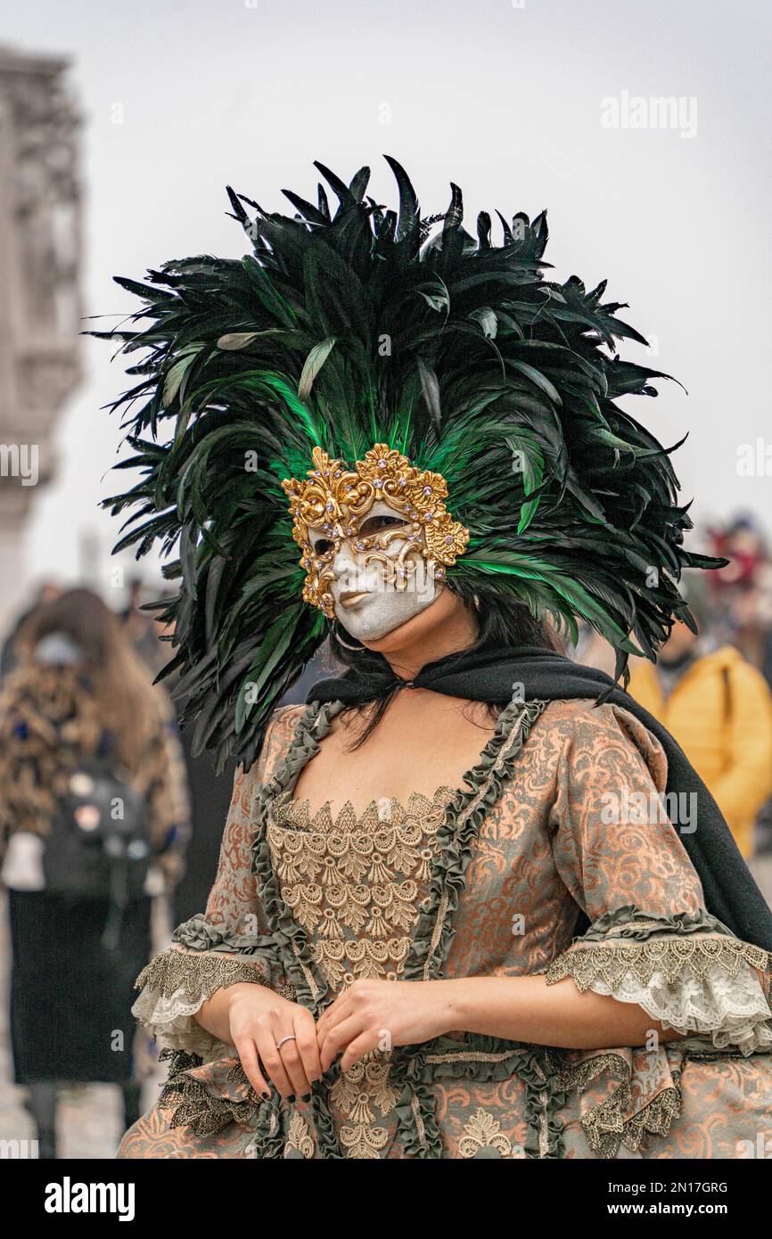 Vinece carnival. A woman in a vintage costume with a lace, wearing a golden carnival mask bordered by a circle of high black feathers, stands alone Stock Photo