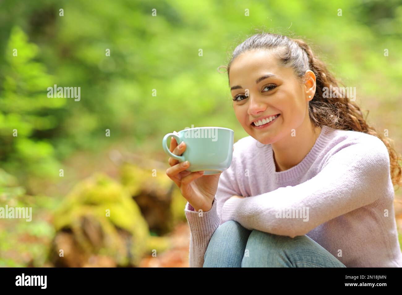Happy woman sitting in nature holding coffee cup posing looking at camera Stock Photo