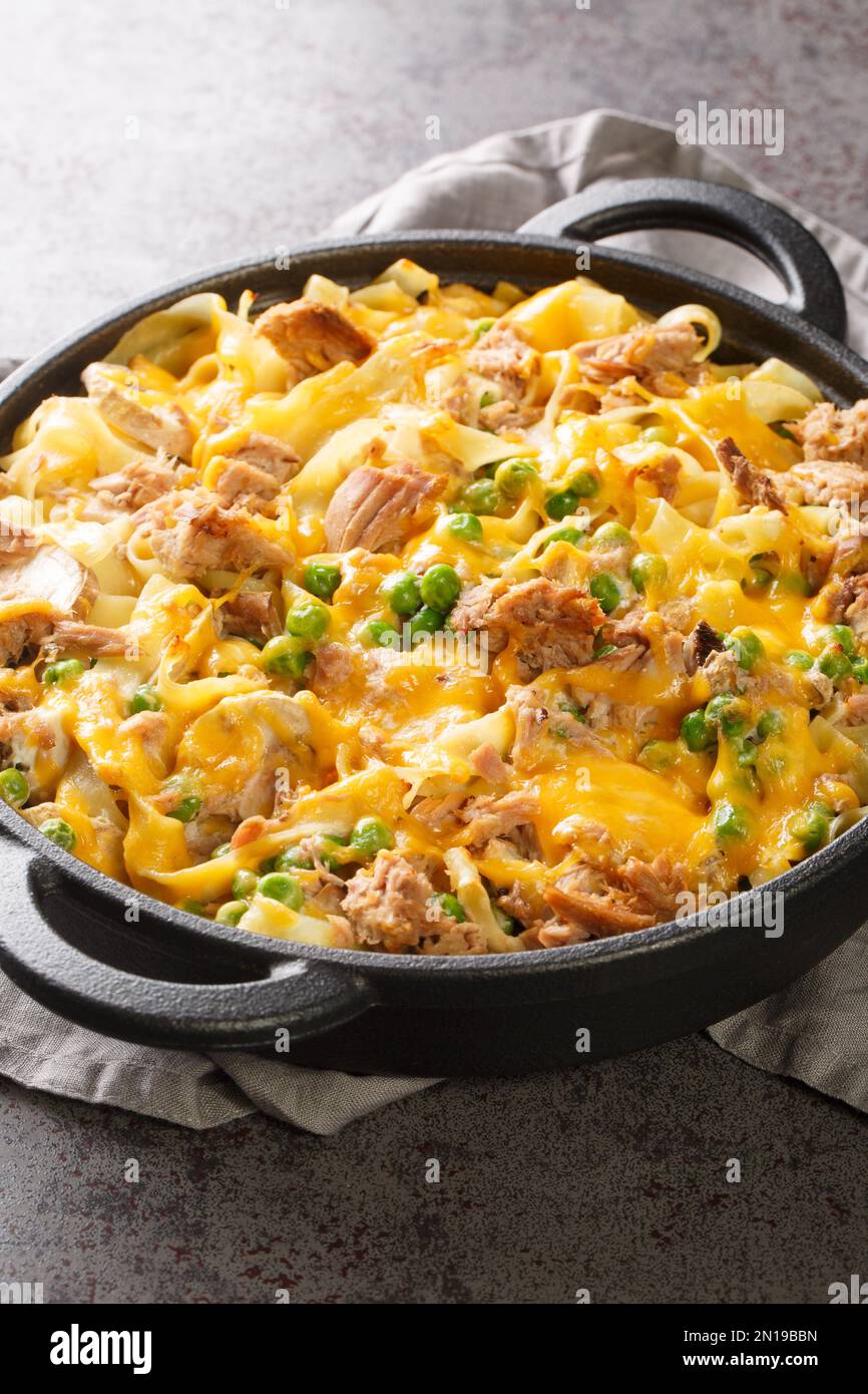 Tuna casserole with noodles, green peas, mushrooms and cheddar cheese close-up in a baking dish on the table. Vertical Stock Photo