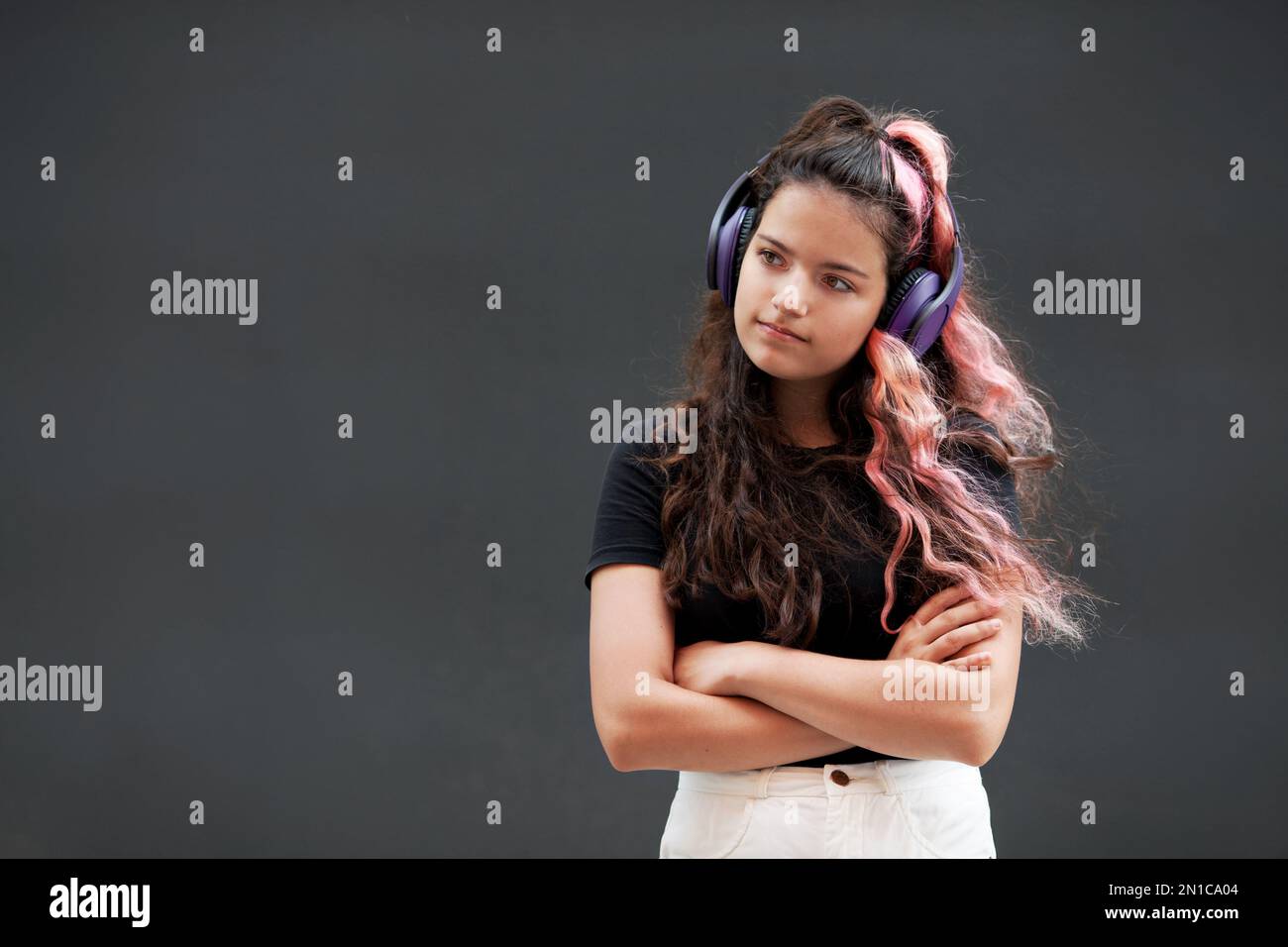 Young Girl with colored long pink hair listen to music with headphones isolated on dark gray background Stock Photo