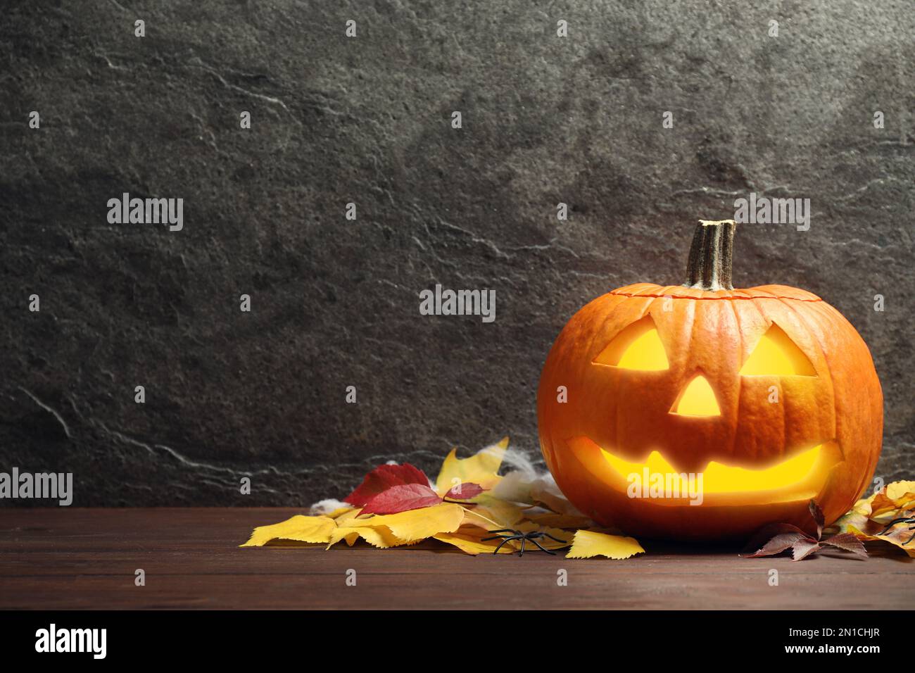 Pumpkin jack o'lantern and autumn leaves on wooden table, space for ...