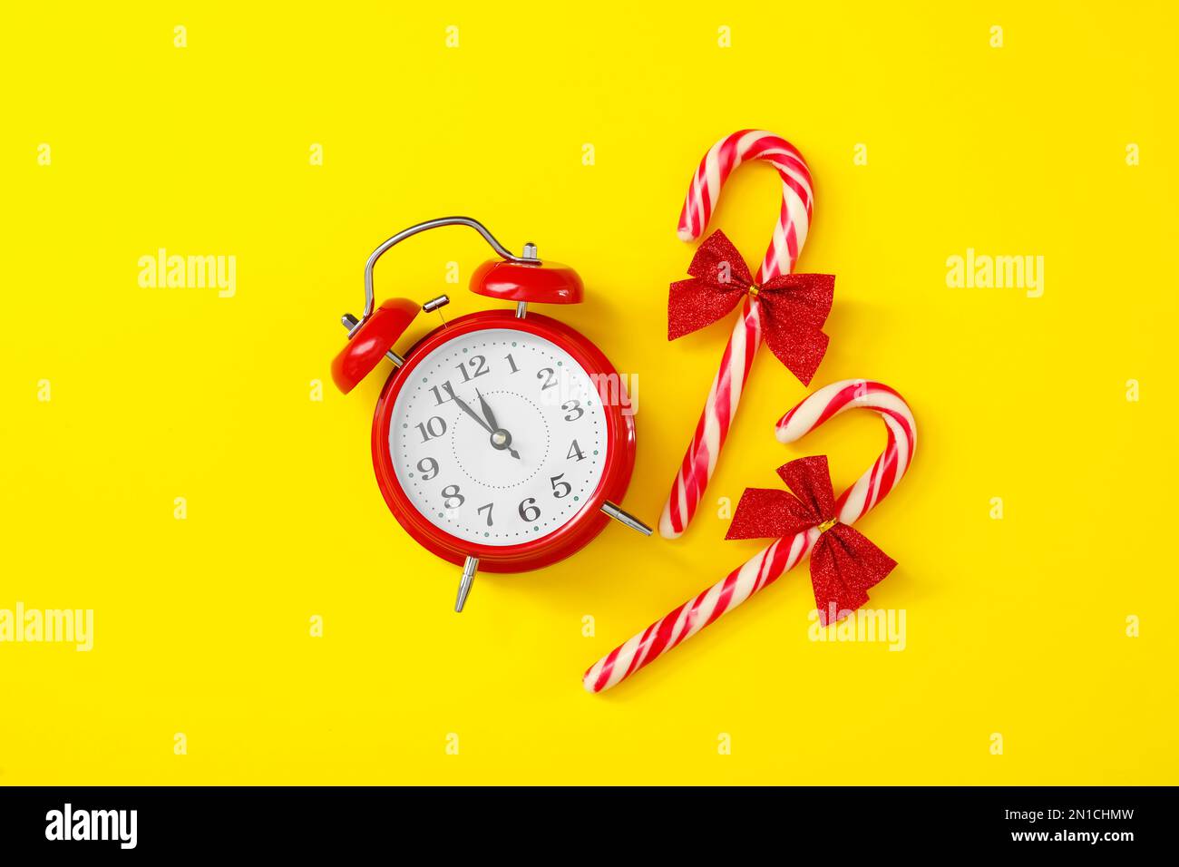Alarm clock and candy canes on yellow background, flat lay. New Year
