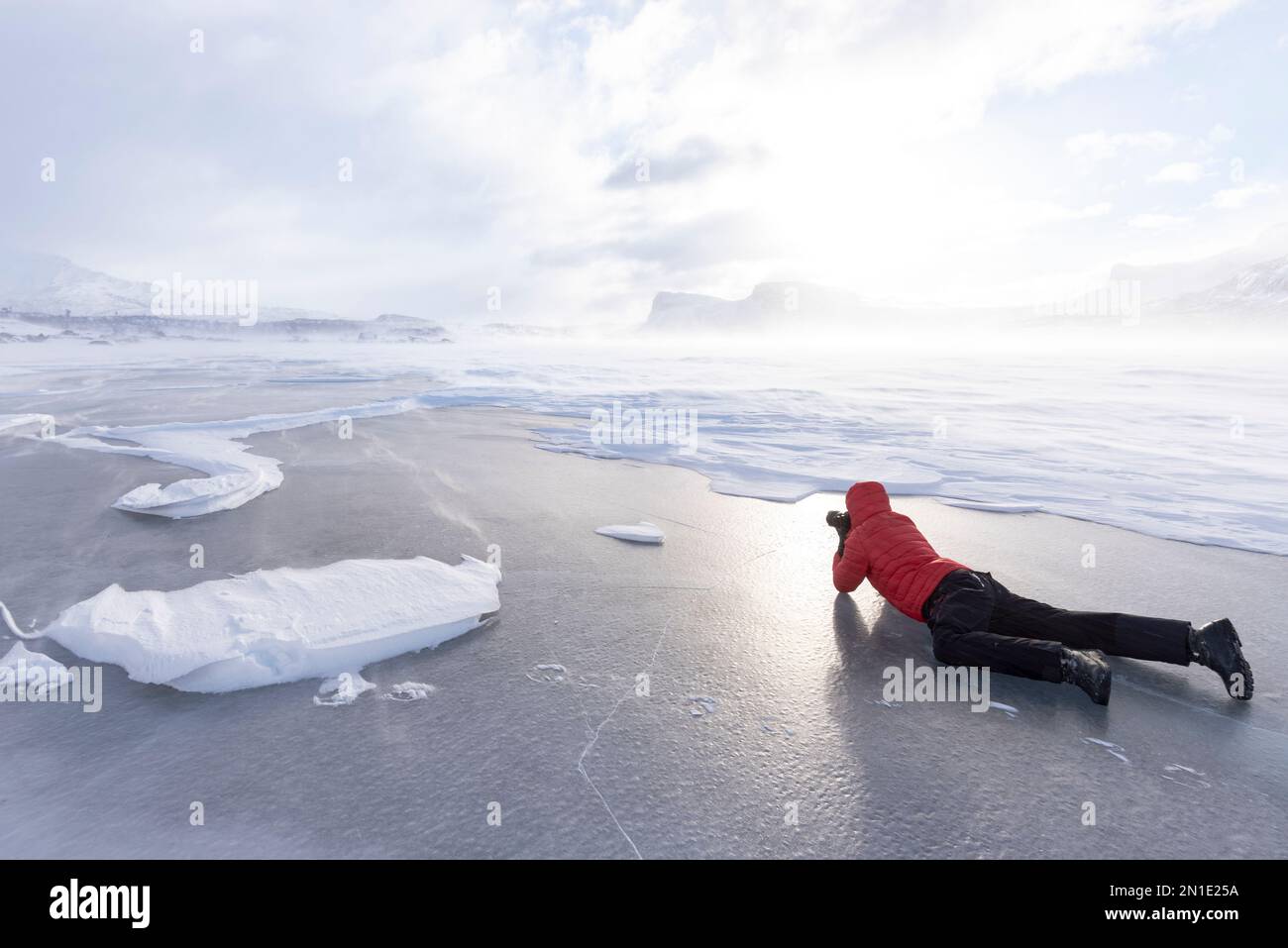 Man photographing the snowy landscape lying down on a frozen lake, Stora Sjofallet, Norrbotten County, Lapland, Sweden, Scandinavia, Europe Stock Photo