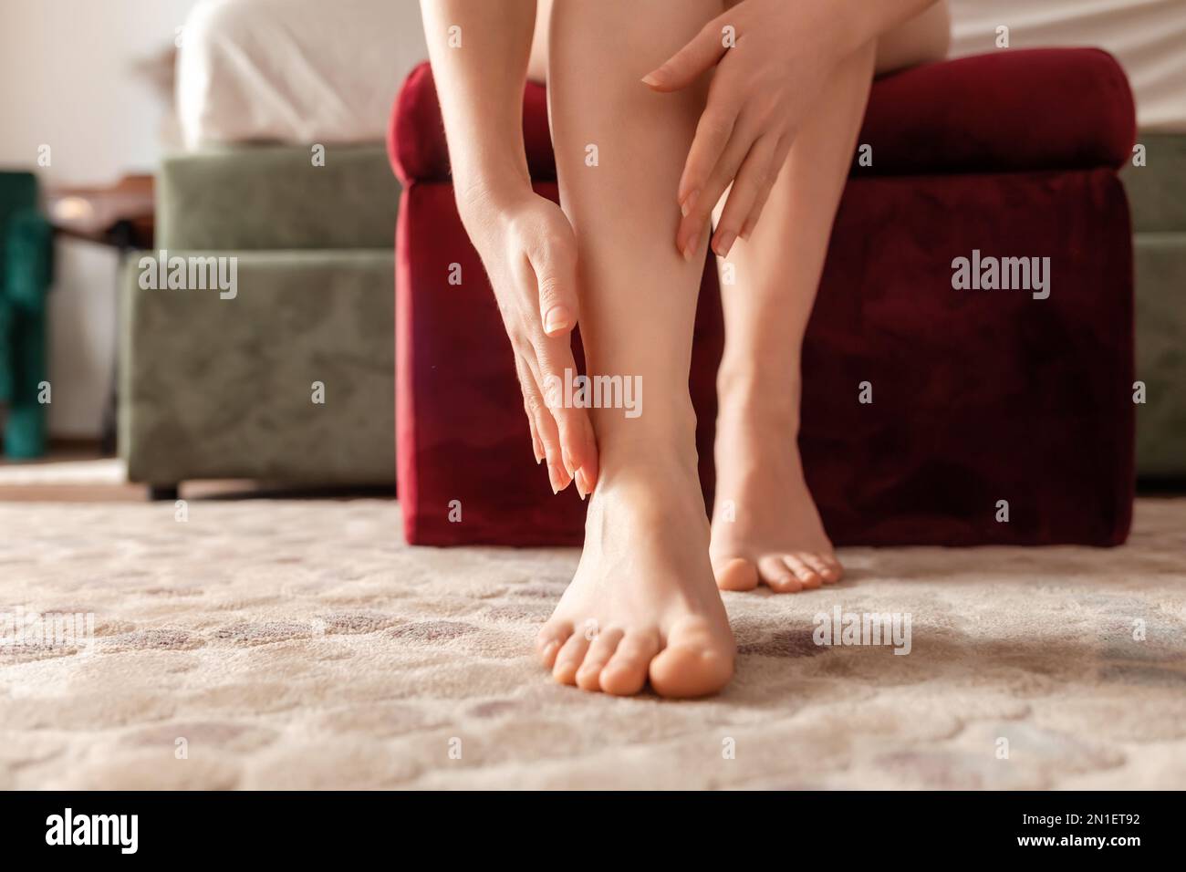 Woman sitting on sofa and massages her barefeet, closeup. Pain and cramps in legs. Concept of