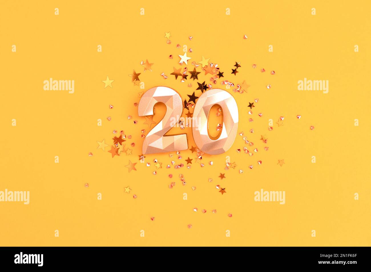 Golden number twenty and stars confetti on a yellow background. Festive glowing compisition. Stock Photo