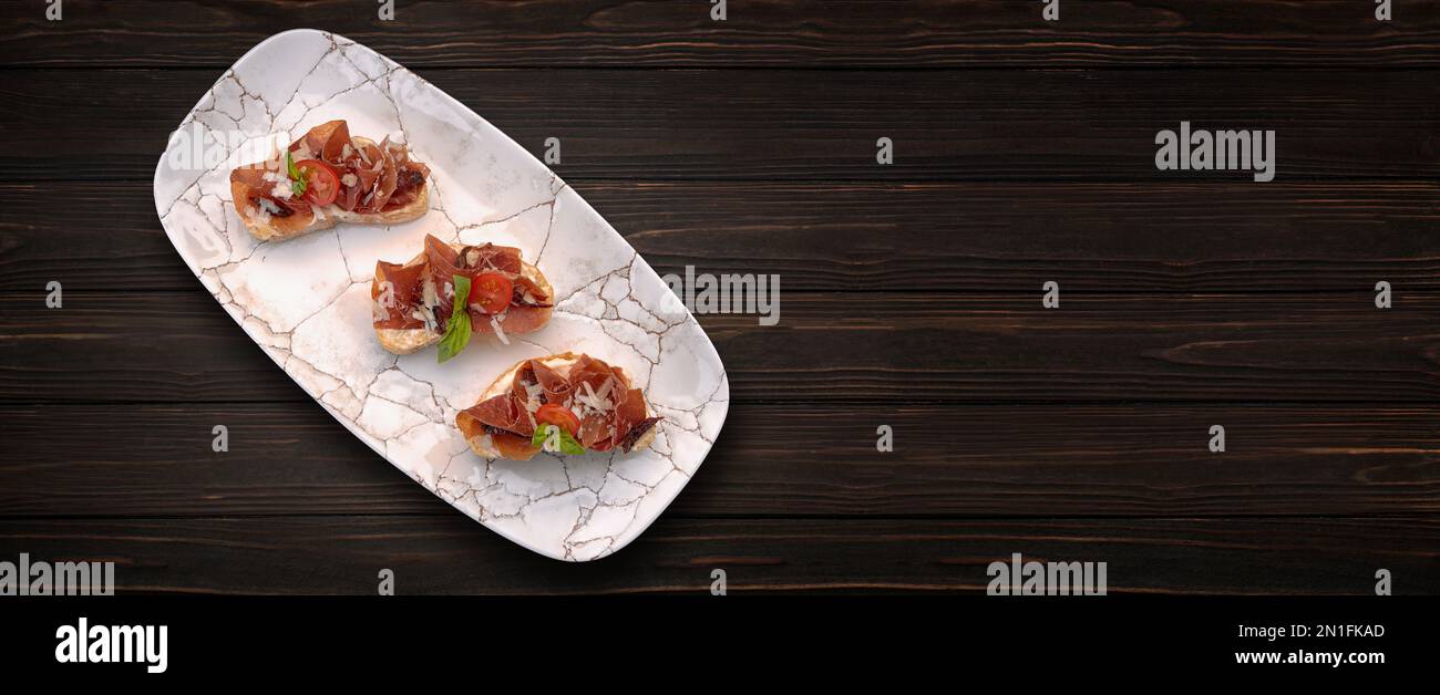 Bruschetta with ham, cheese and tomatoes, on a wooden background. Banner Stock Photo