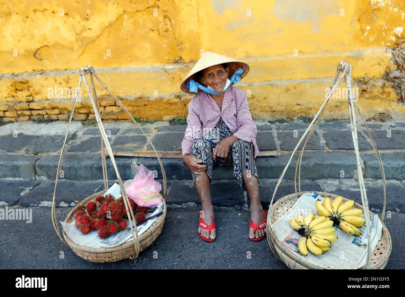 Typical street vendor with Vietnamese hat sitting down selling food, fresh fruit, Hoi An, Vietnam, Indochina, Southeast Asia, Asia Stock Photo