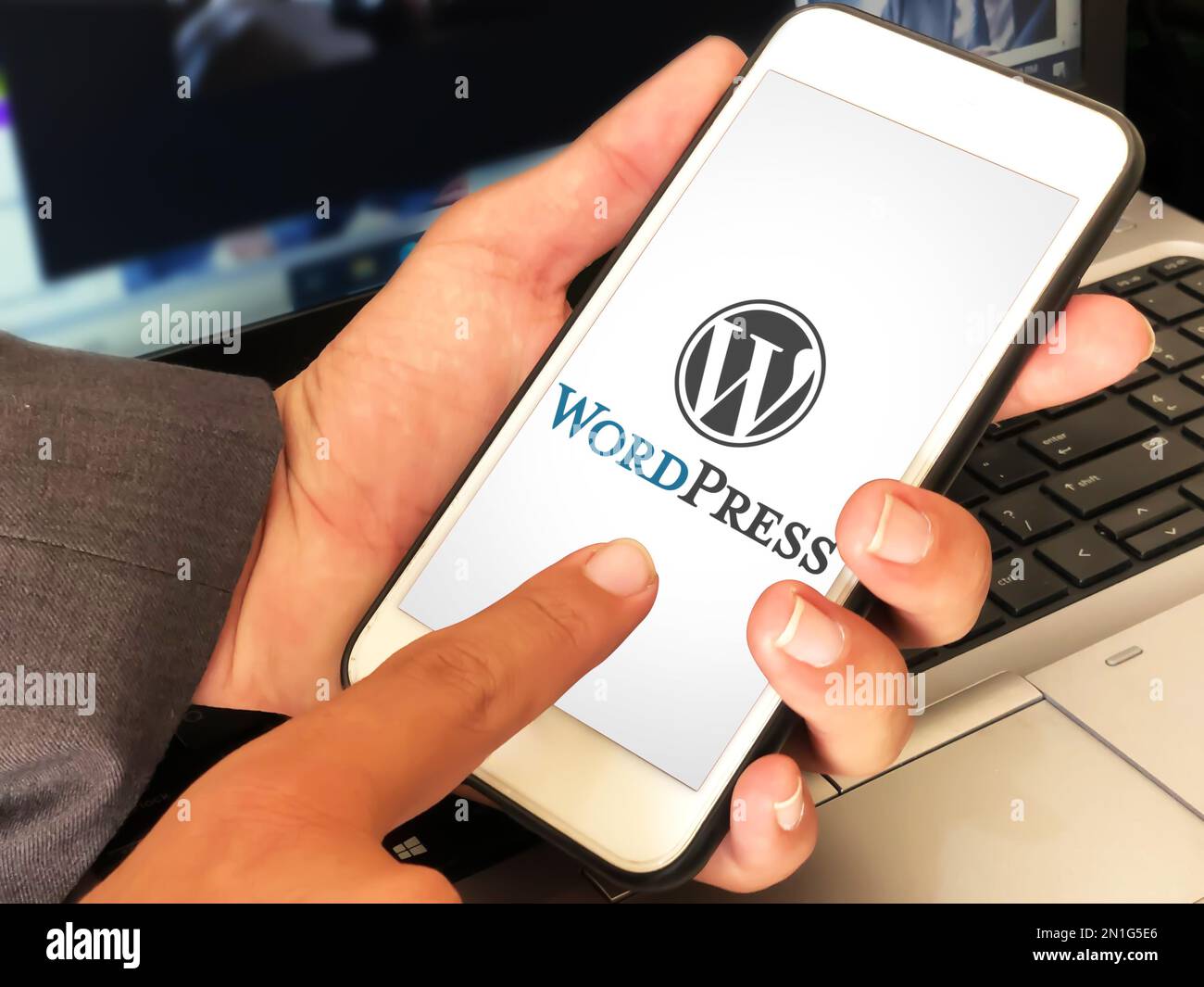 Man using wordpress application on mobile with laptop in the backdrop