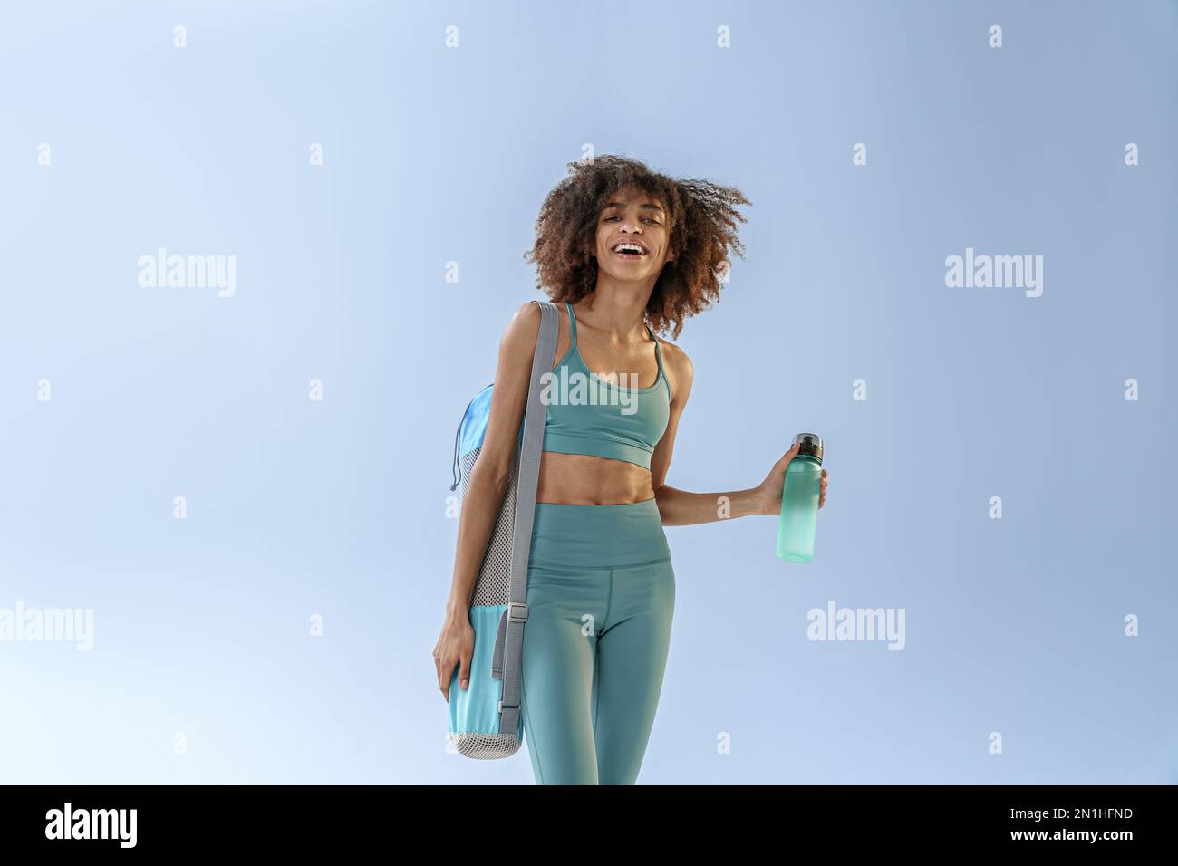 Smiling sporty woman with sports bag and bottle of water after training ...