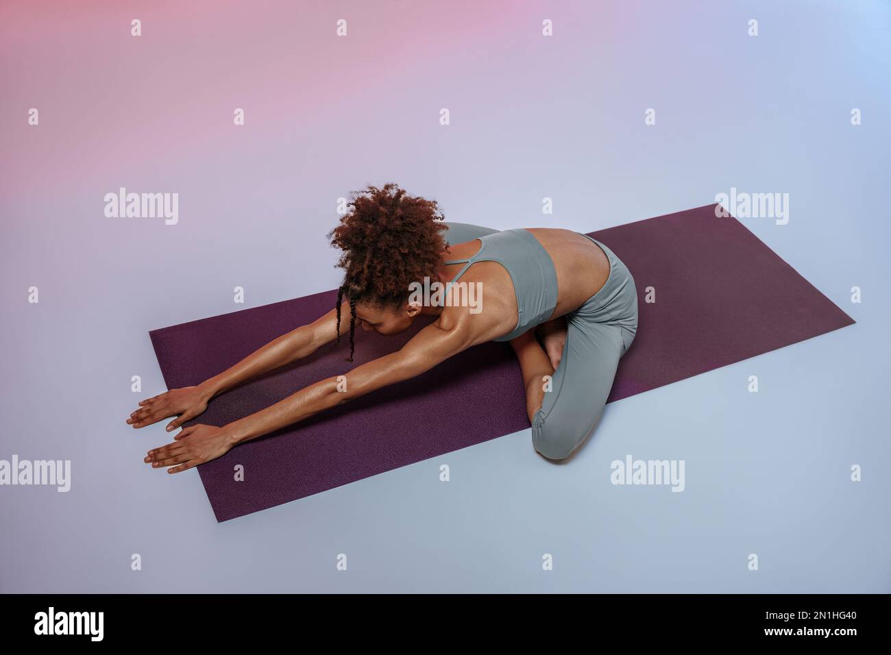 Sporty woman doing stretching exercises on yoga mat on studio