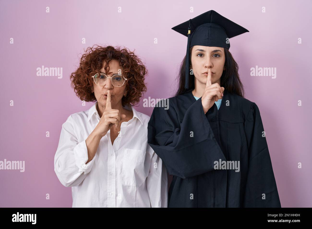 Hispanic mother and daughter wearing graduation cap and ceremony robe ...
