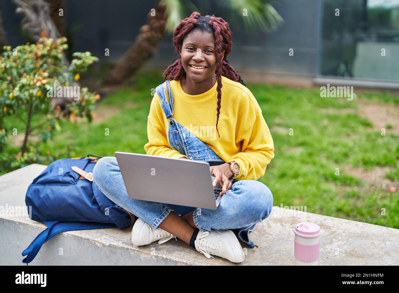 African american woman student using laptop sitting on bench at campus ...