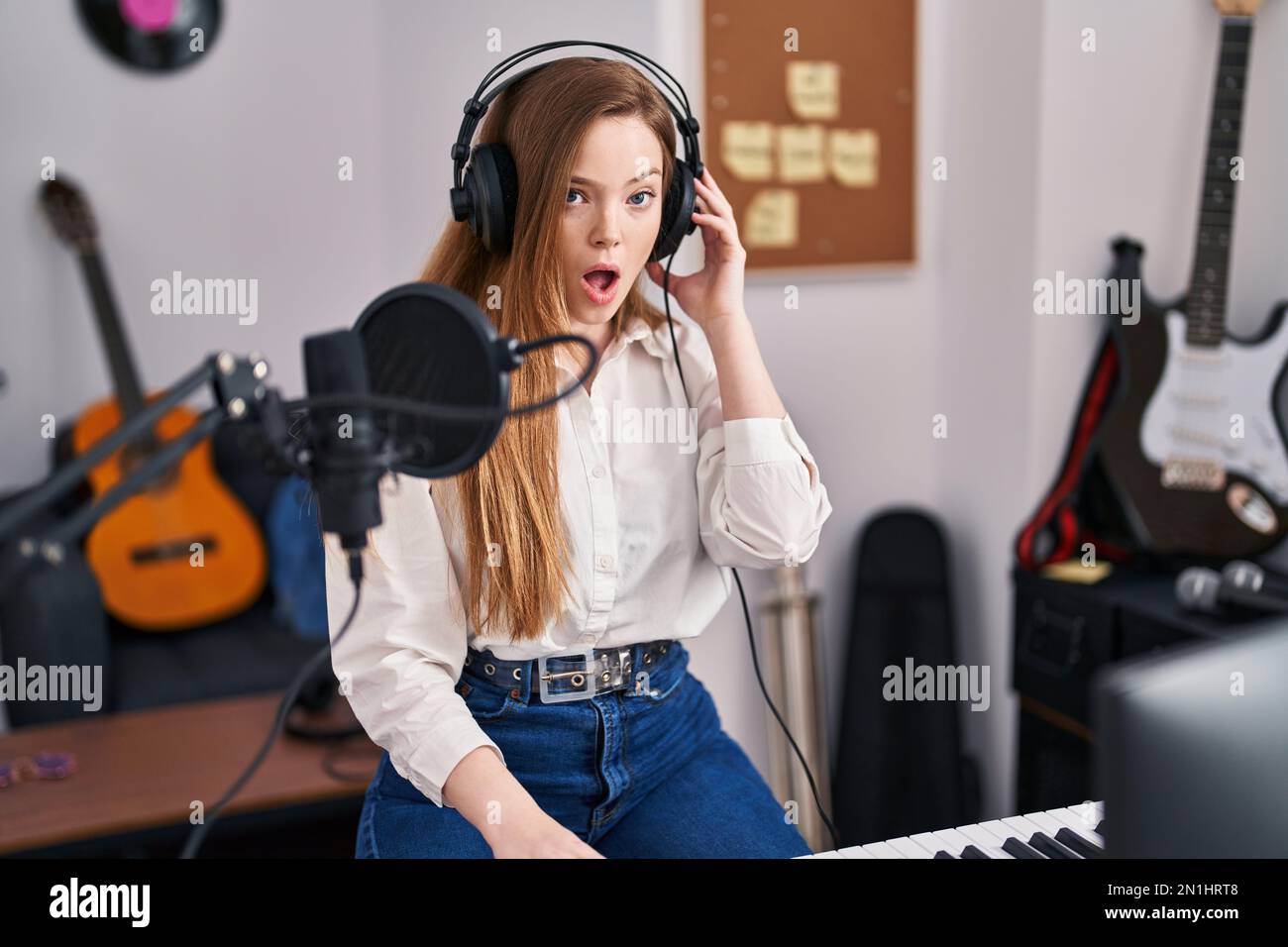 Young caucasian woman recording song at music studio scared and amazed with open mouth for surprise, disbelief face Stock Photo