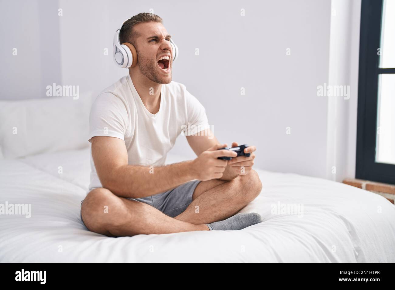 Young caucasian man sitting on the bed at home playing video games ...