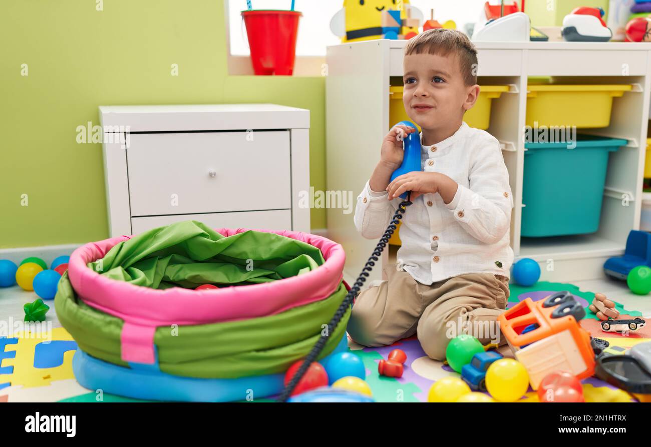 Adorable caucasian boy playing with telephone toy sitting on floor at ...