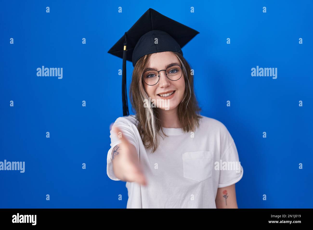 Blonde caucasian woman wearing graduation cap smiling friendly offering ...