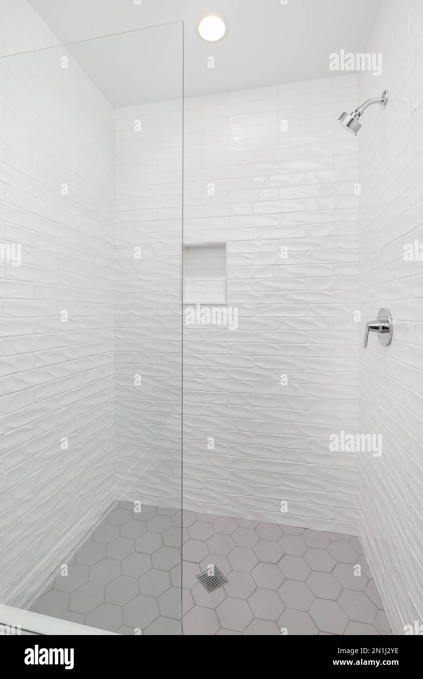 A walkin shower with white wavy subway tiles, a grey hexagon tiled