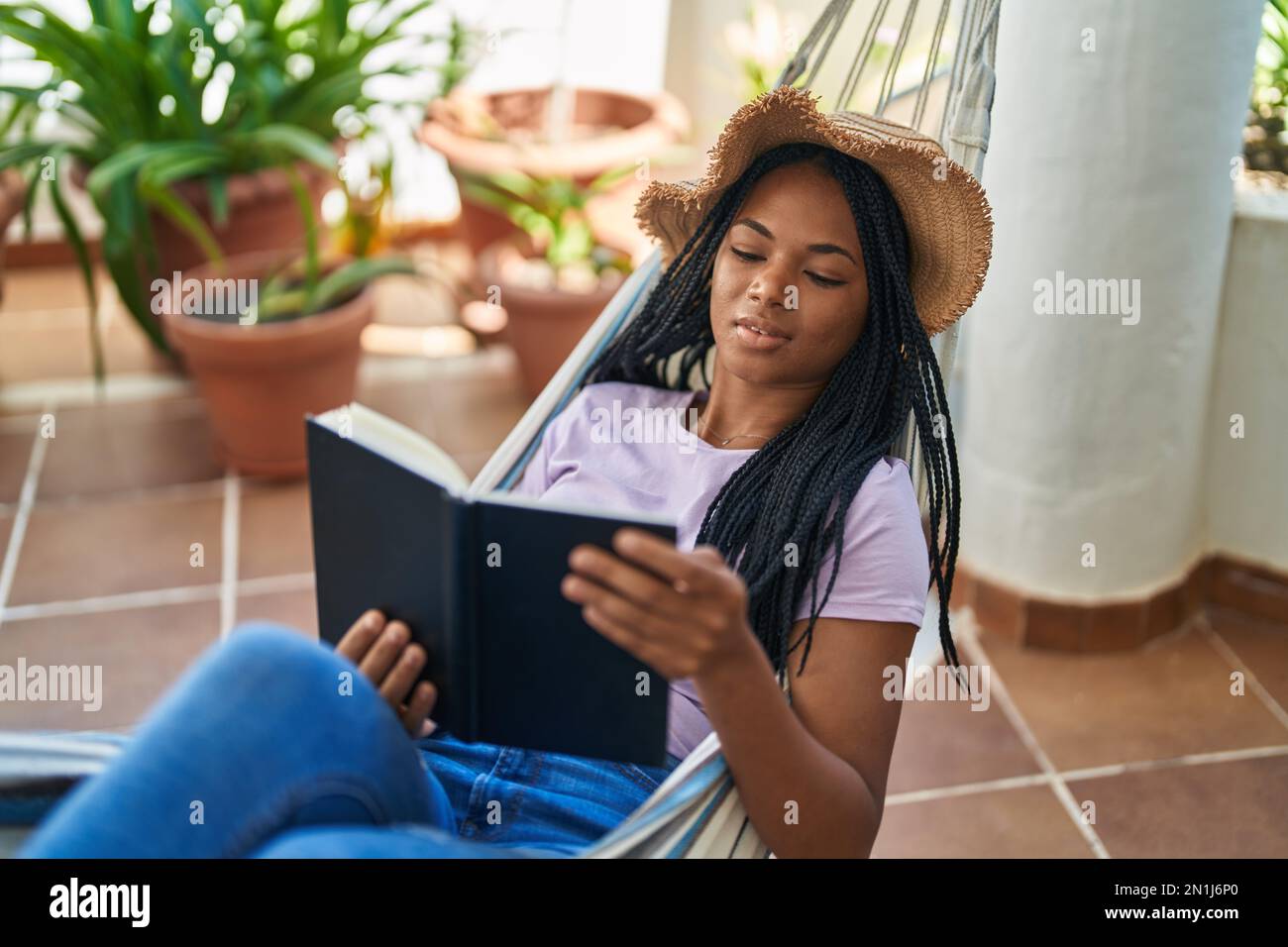 African american woman reading book lying on hammock at home terrace ...