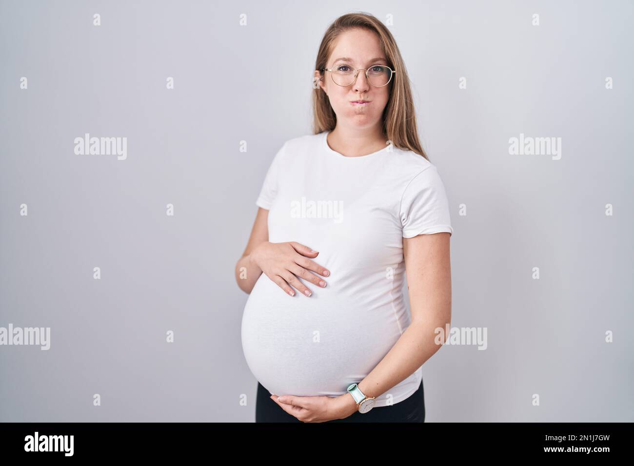 Young pregnant woman expecting a baby, touching pregnant belly puffing