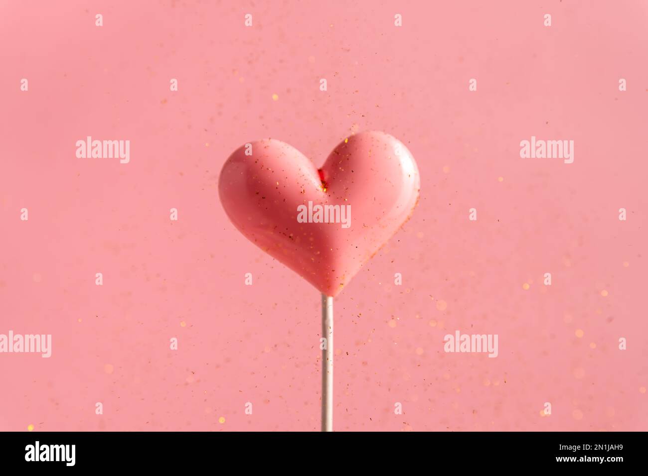 Pink Valentine's day heart shape lollipop candy on empty pastel pink background with golden flying sequins. Love Concept. Minimalism colorful style Stock Photo