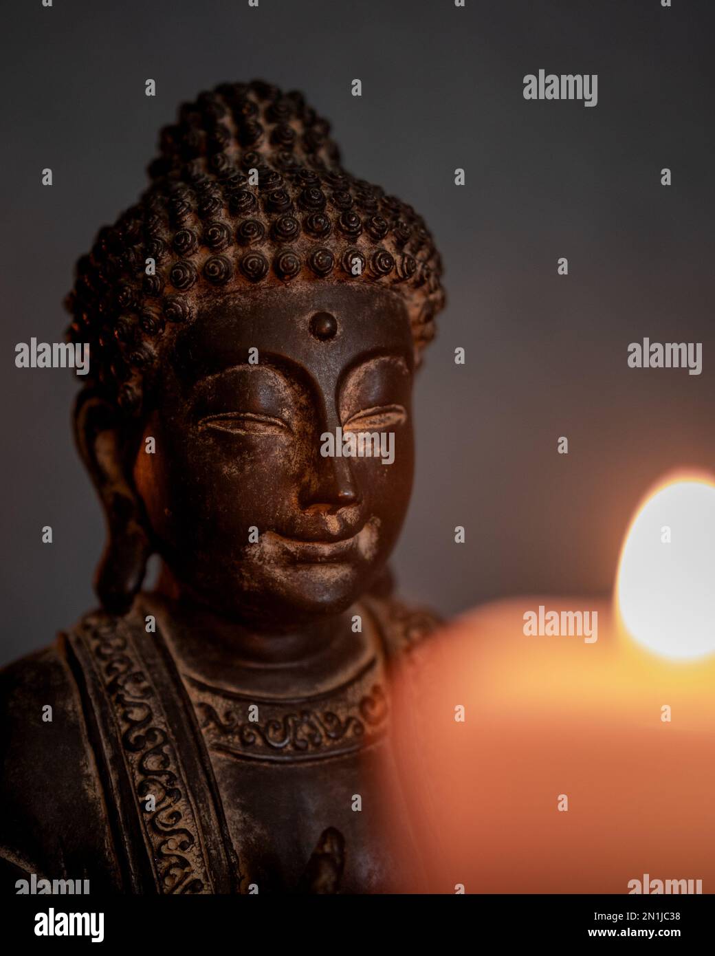 Close-up of the statue of Buddha with selective focus and blurred candlelight in the foreground. Buddhism concept Stock Photo