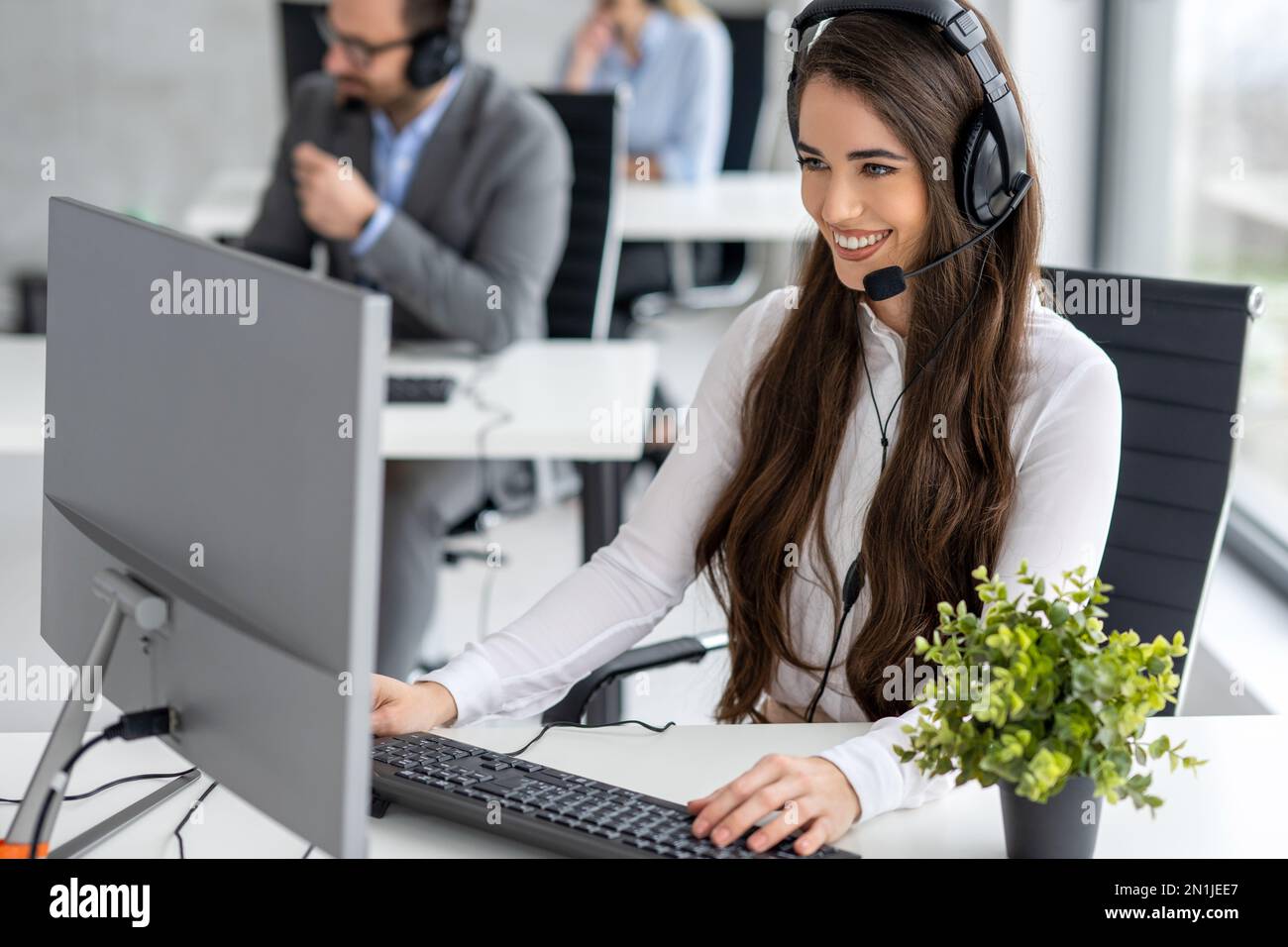 Call center worker accompanied by her team working with a headset at office. Stock Photo