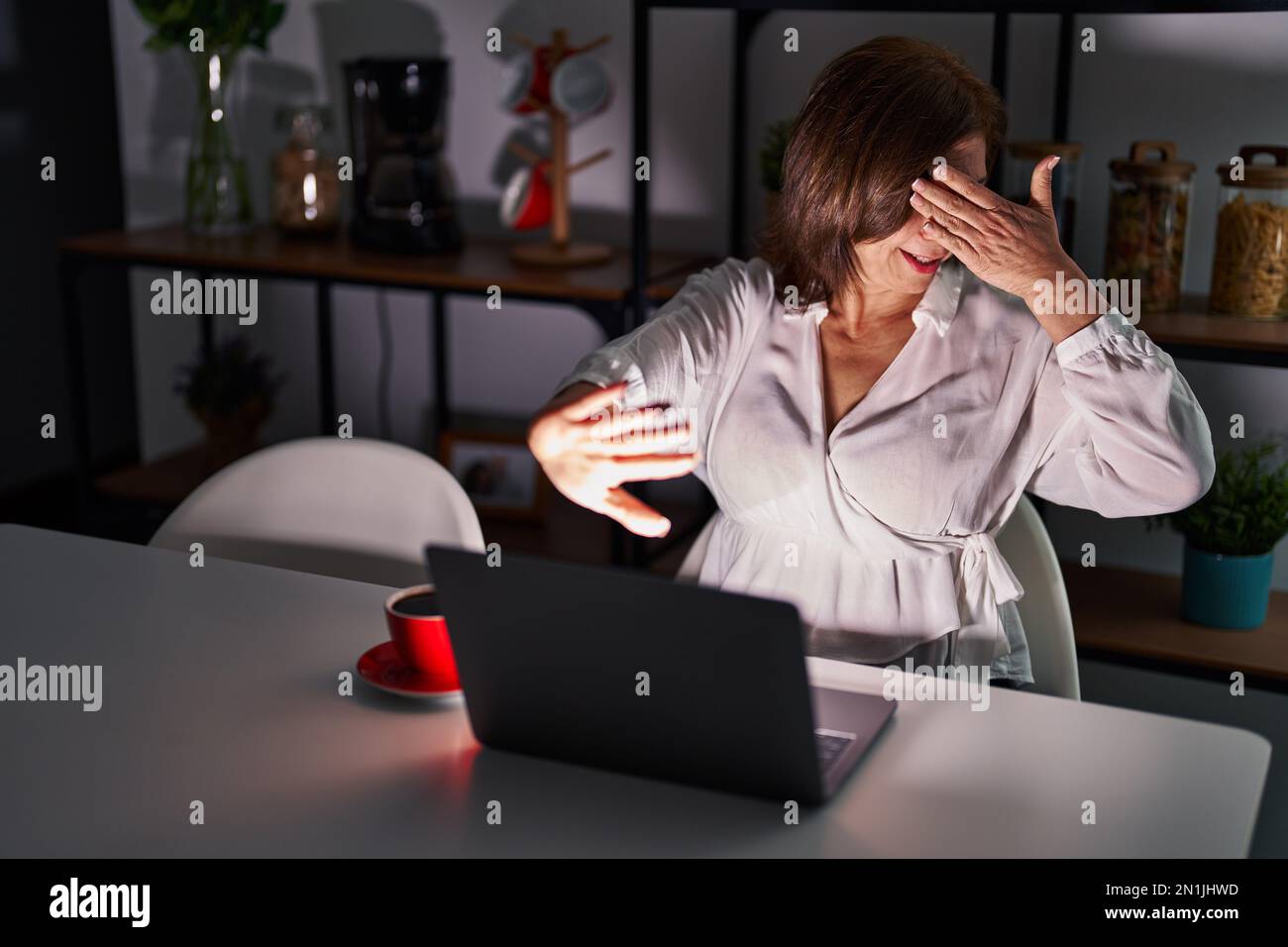 Middle age hispanic woman using laptop at home at night covering eyes with hands and doing stop gesture with sad and fear expression. embarrassed and Stock Photo