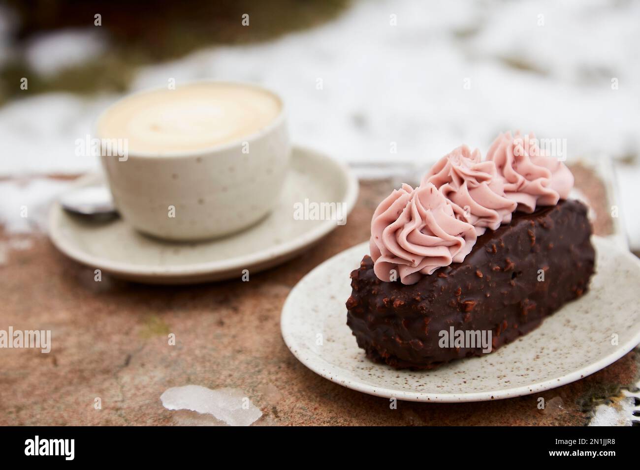 Aestetics vegan brownie witn no sugar cake dessert and cup of cappuccino outdoor at the snowy day. Coffee with dessert winter aesthetics. Stock Photo
