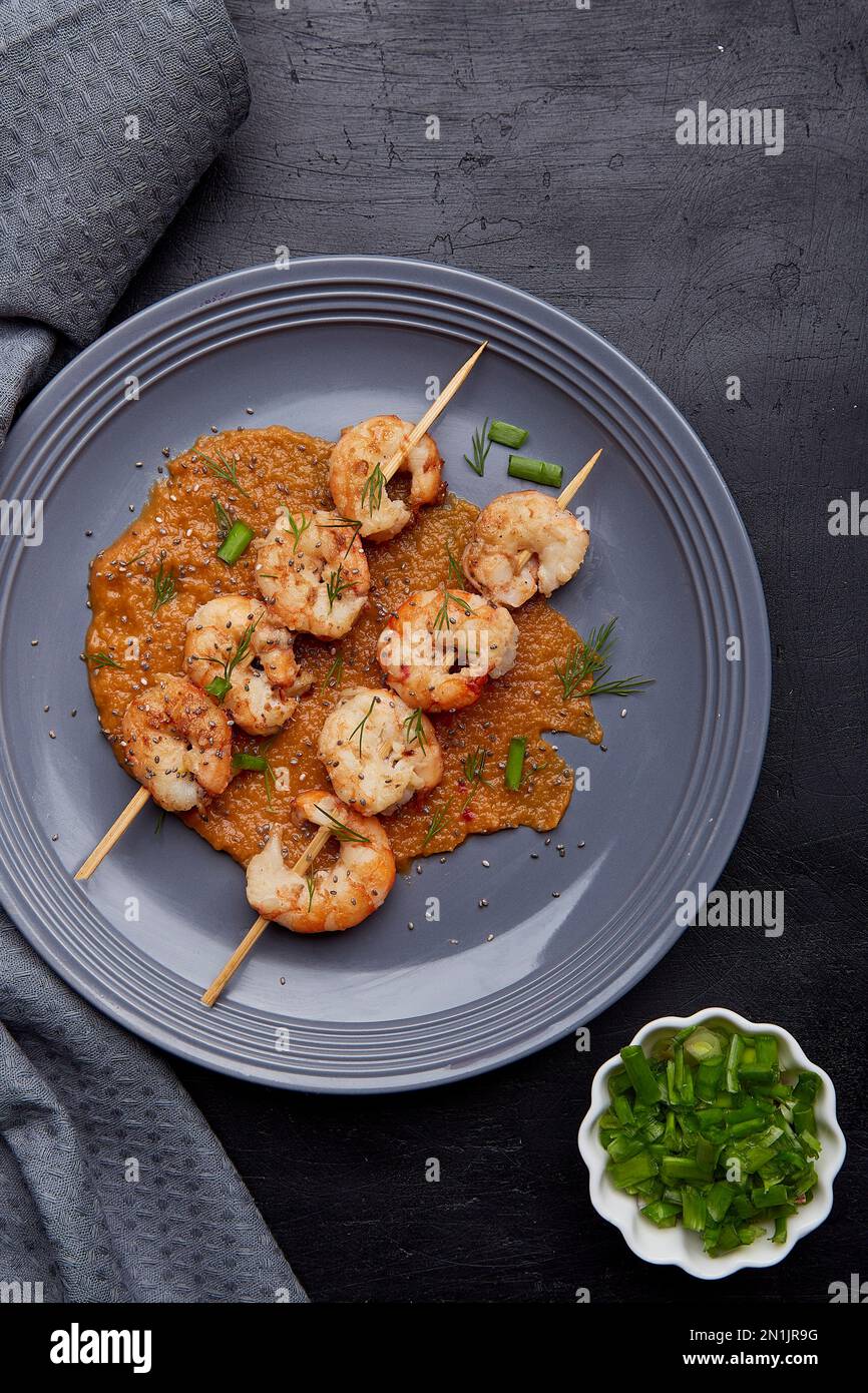 Party snacks. Grilled shrimps on skewers on the plate close up. Seafood barbecue, roast prawns flat lay. Stock Photo