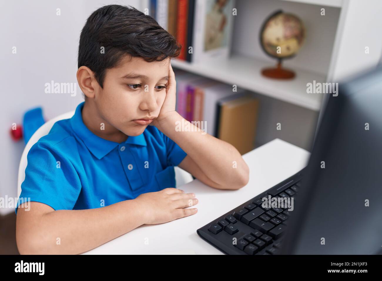 Adorable hispanic boy student using computer with tired expression at ...