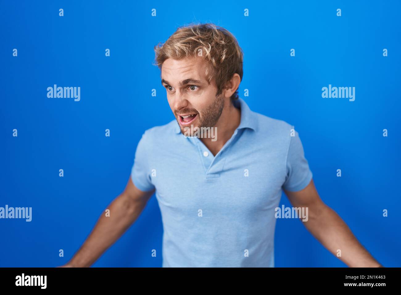 Caucasian man standing over blue background angry and mad screaming ...