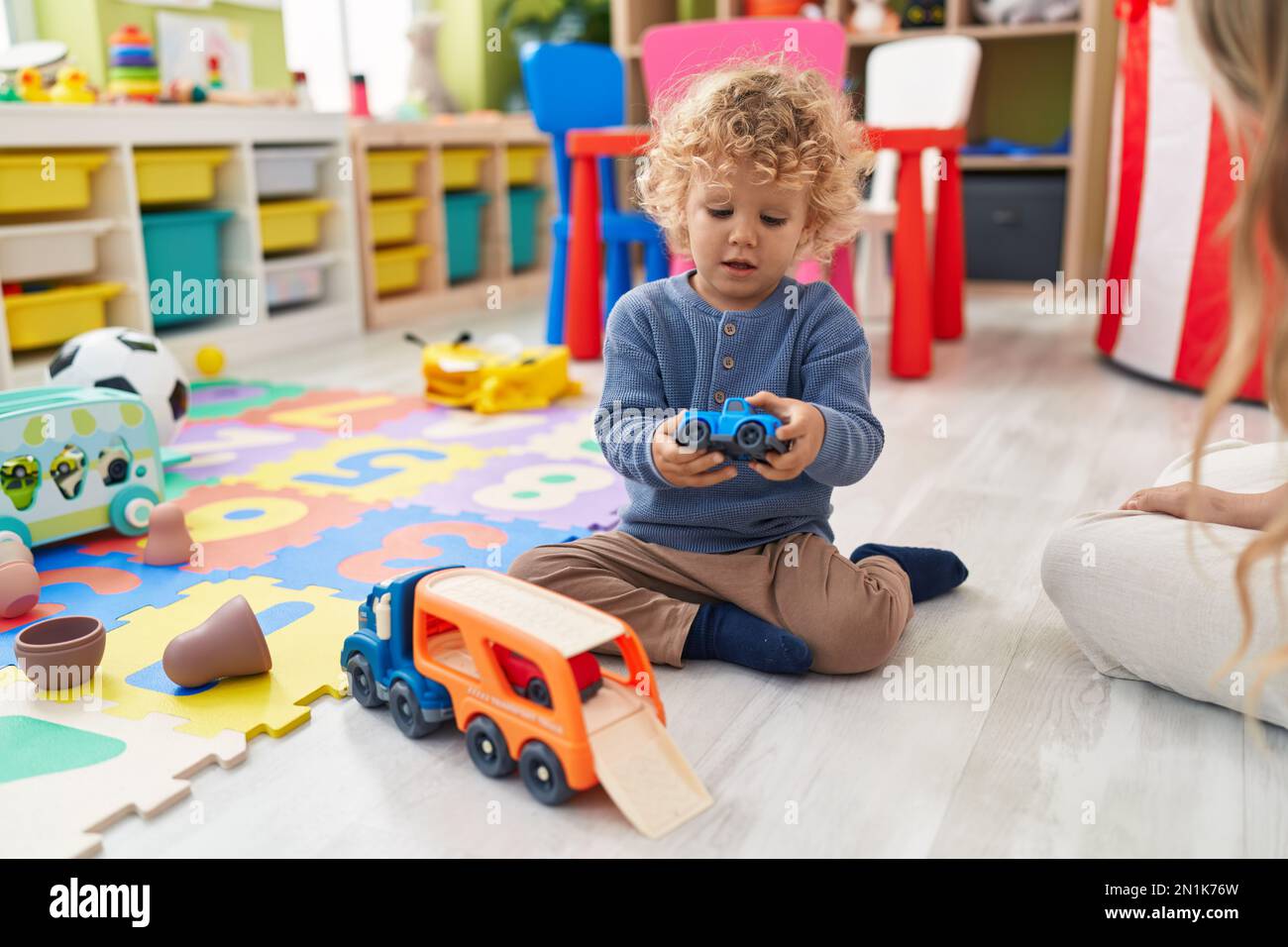 Adorable blond toddler playing with cars toy sitting on floor at ...