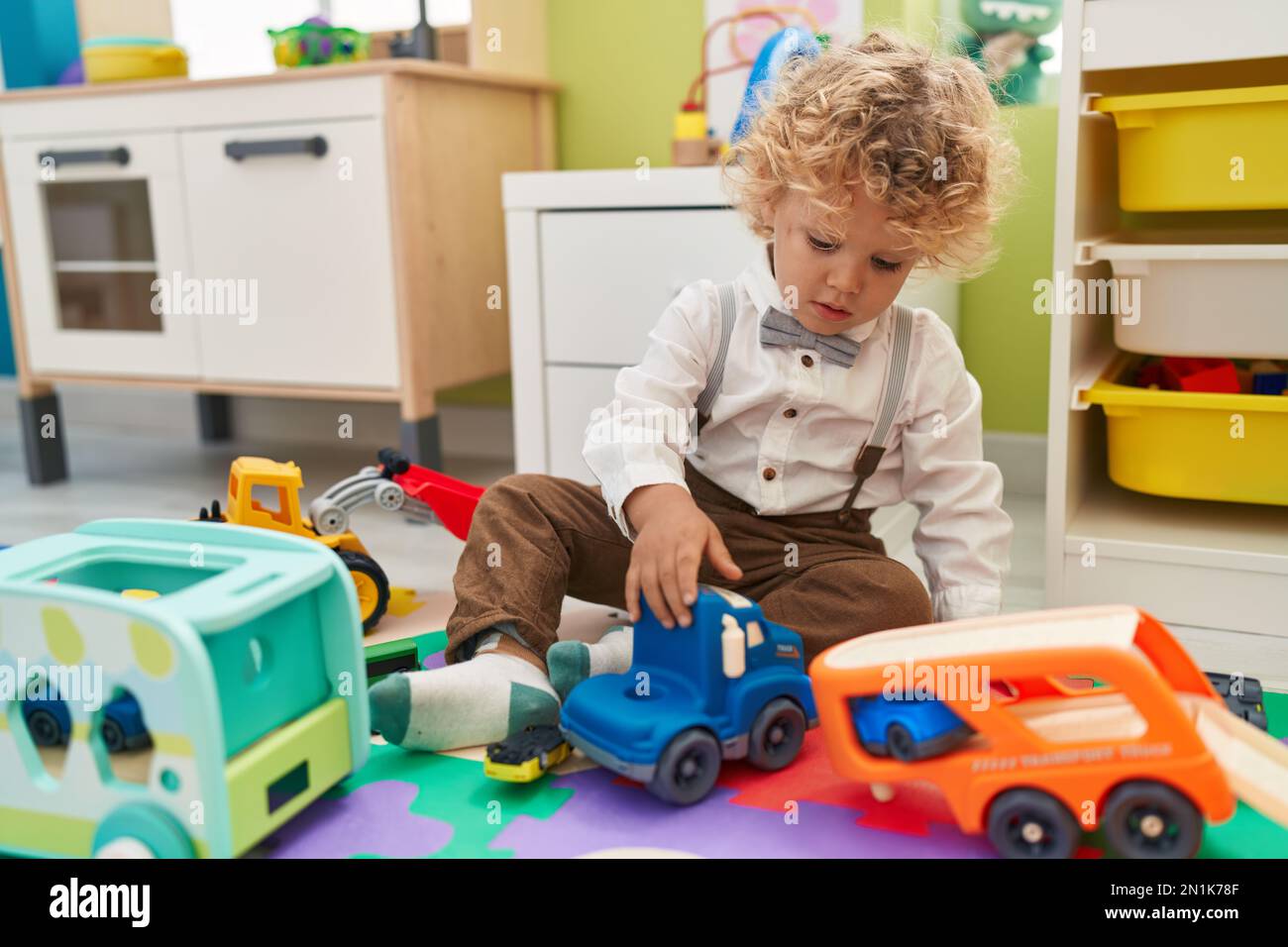 Adorable blond toddler playing with cars toy sitting on floor at ...
