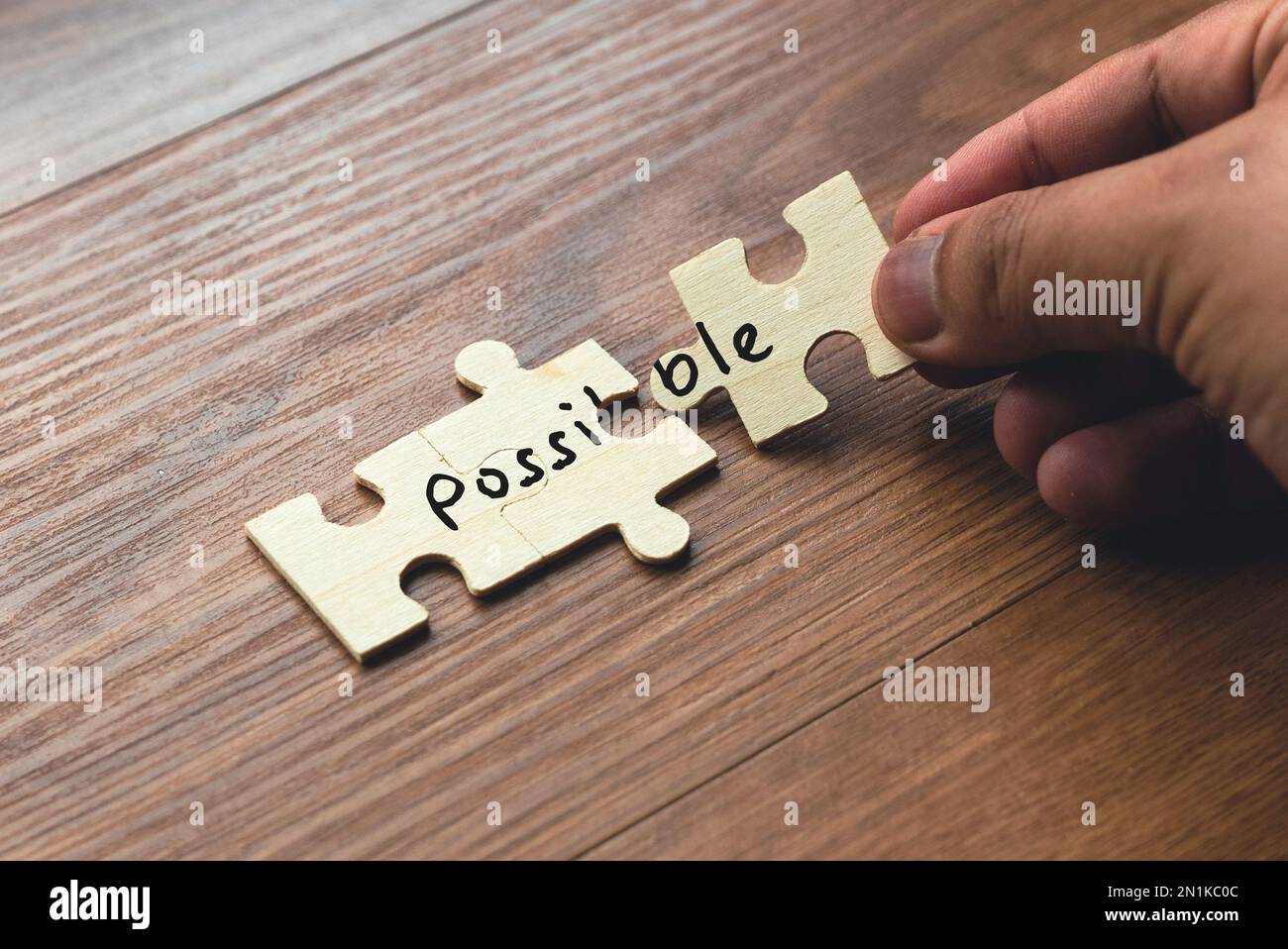 A hand holding puzzle pieces with word possible spread over two section. Concept of problem solving and overcoming challenges. Stock Photo